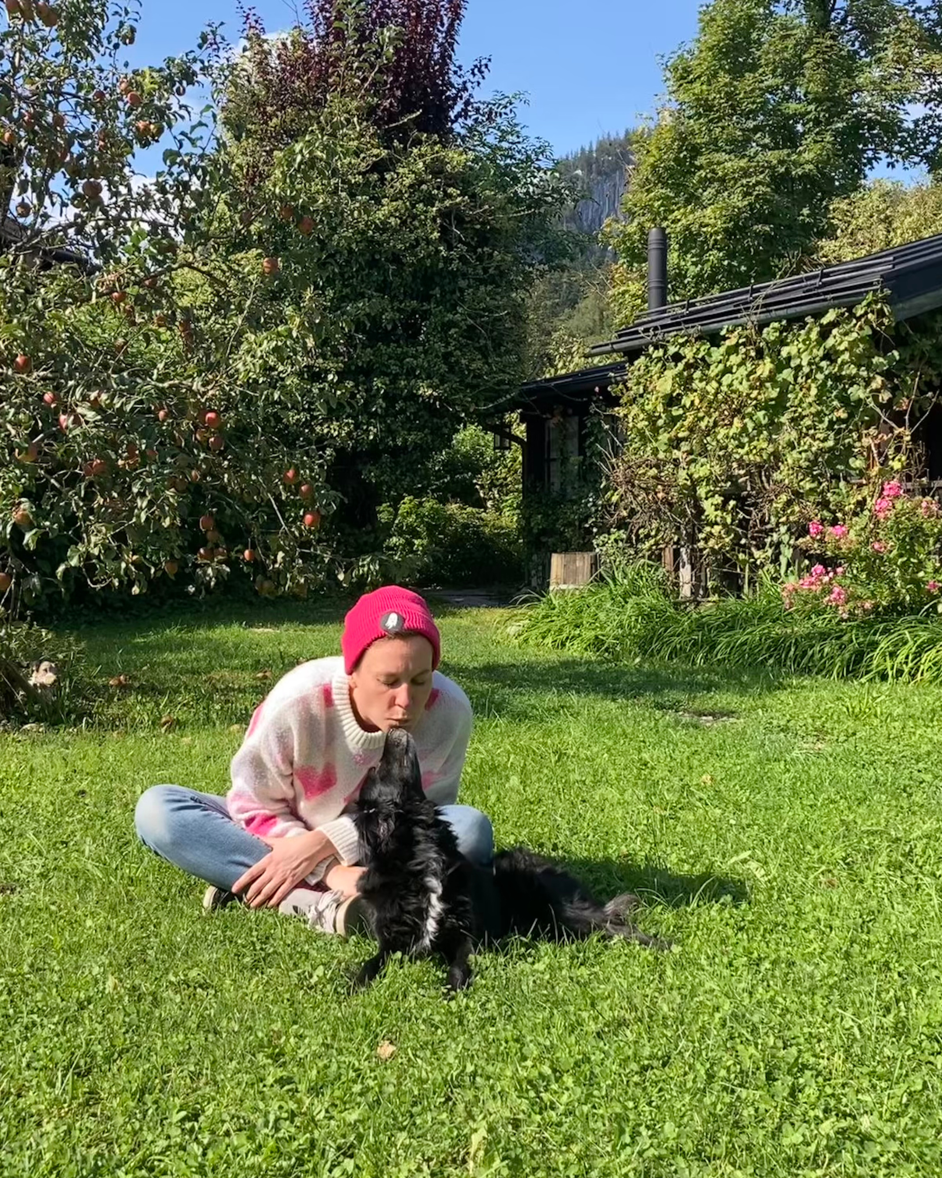 Eine Frau sitzt im Gras und kuschelt mit einem Hund